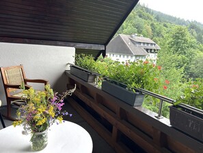A balcony with a wooden chair, a white table with a vase of flowers, and potted plants.