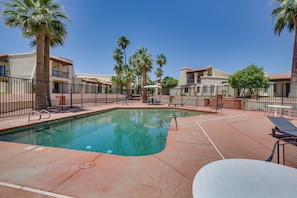A swimming pool with a tiled deck, surrounded by a fence, palm trees, and buildings with balconies. - Yuma Desert Oasis: Pool & Remote Work Setup! (Yuma)