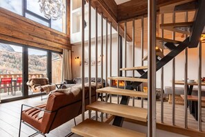 Ein modernes Interieur mit einer Holztreppe, einer Couch und einem Essbereich mit Blick ins Freie.