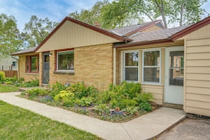 A single-story house with a front porch, a small garden with various plants, and a visible garage door. - Huge Yard, Fire Pit, Garden! Milwaukee Family Home (Milwaukee)