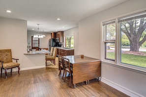 A spacious dining area with a wooden table and chairs, a kitchen in the background, and a large window with a view of a tree. - Huge Yard, Fire Pit, Garden! Milwaukee Family Home (Milwaukee)