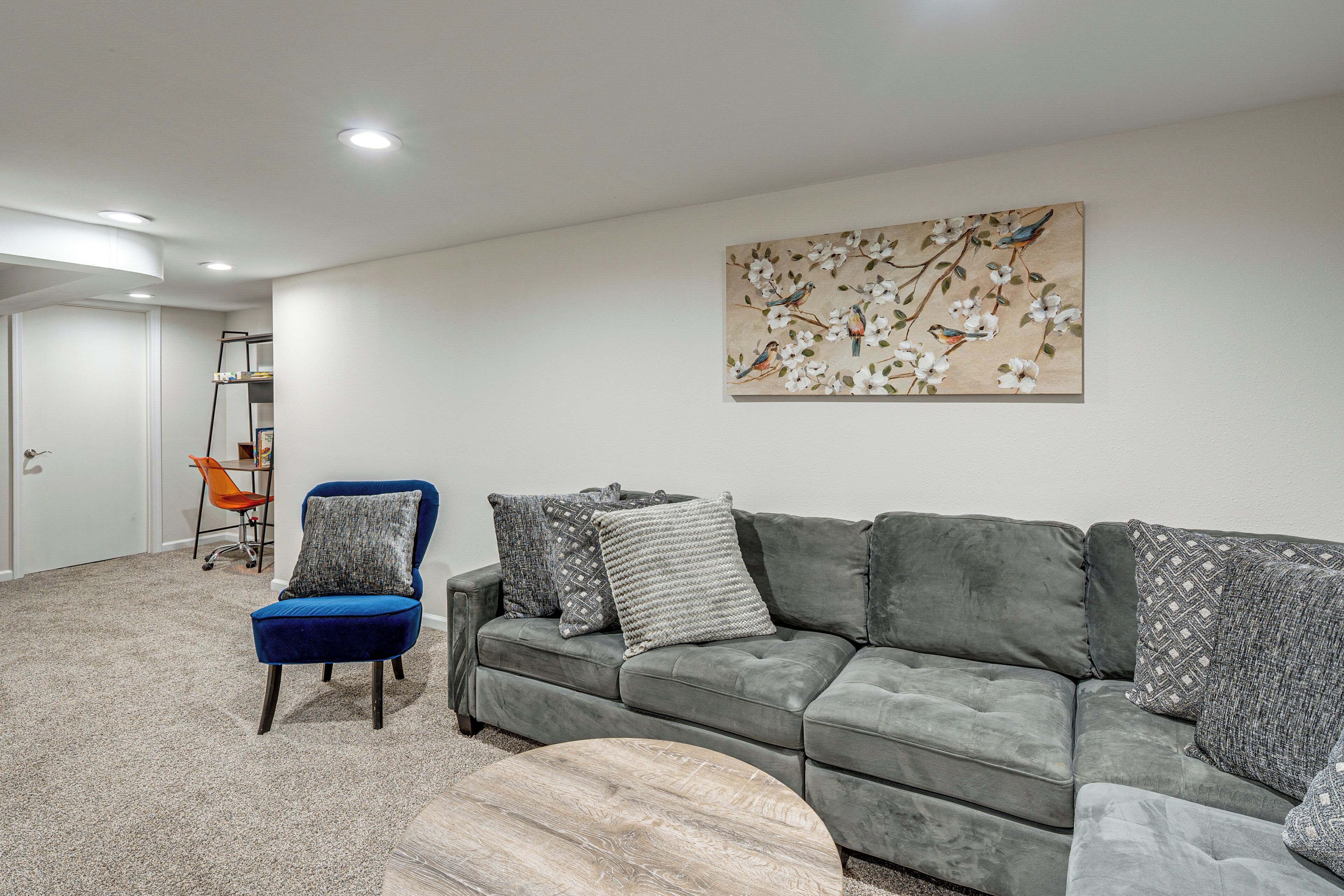 A living room with a grey sofa, a blue chair, a coffee table, and a painting of birds on the wall.