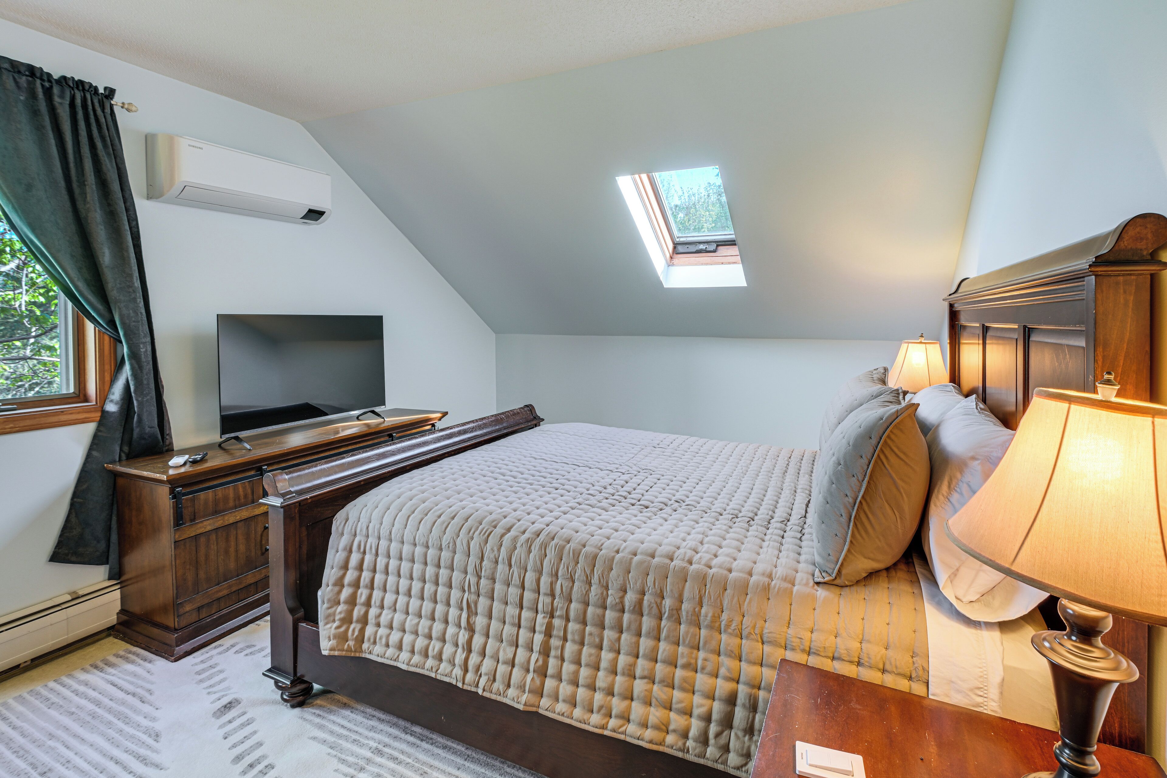 Un dormitorio con una cama, un escritorio, un televisor, una lámpara y un tragaluz.