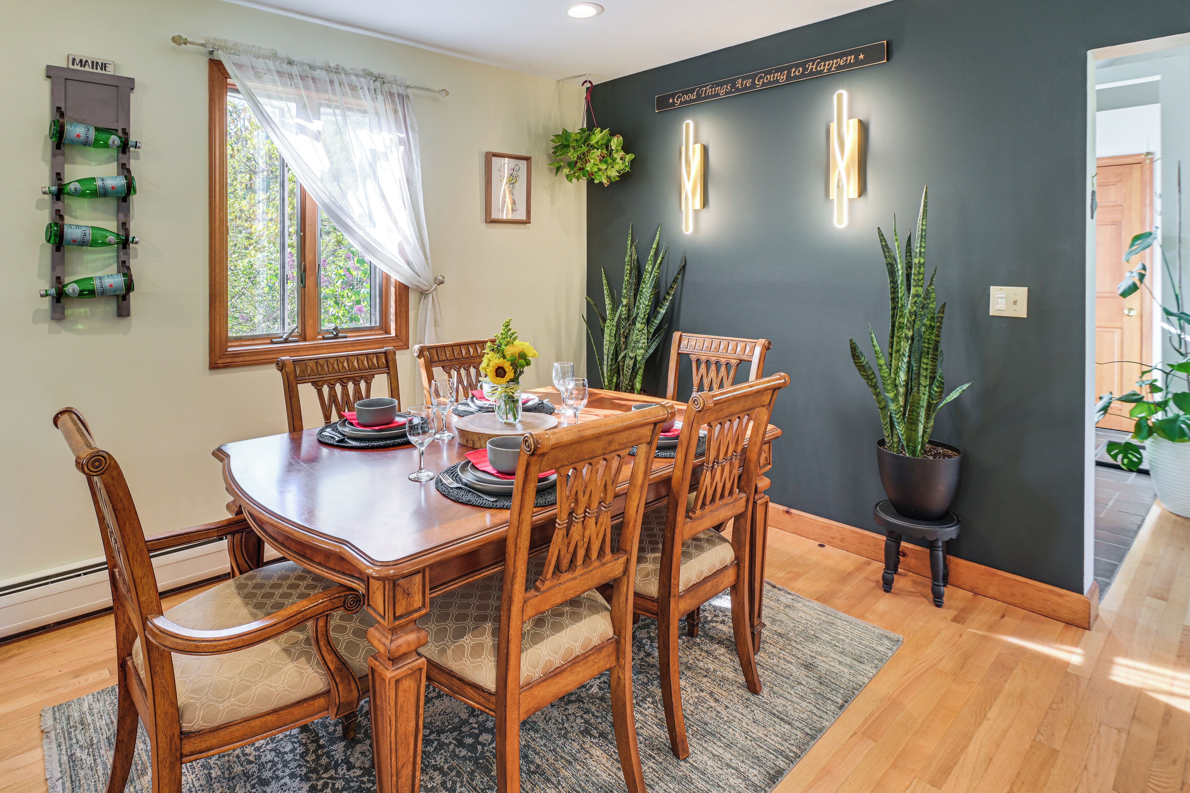 Un comedor con una mesa de madera, sillas, una planta en maceta y un letrero en la pared.
