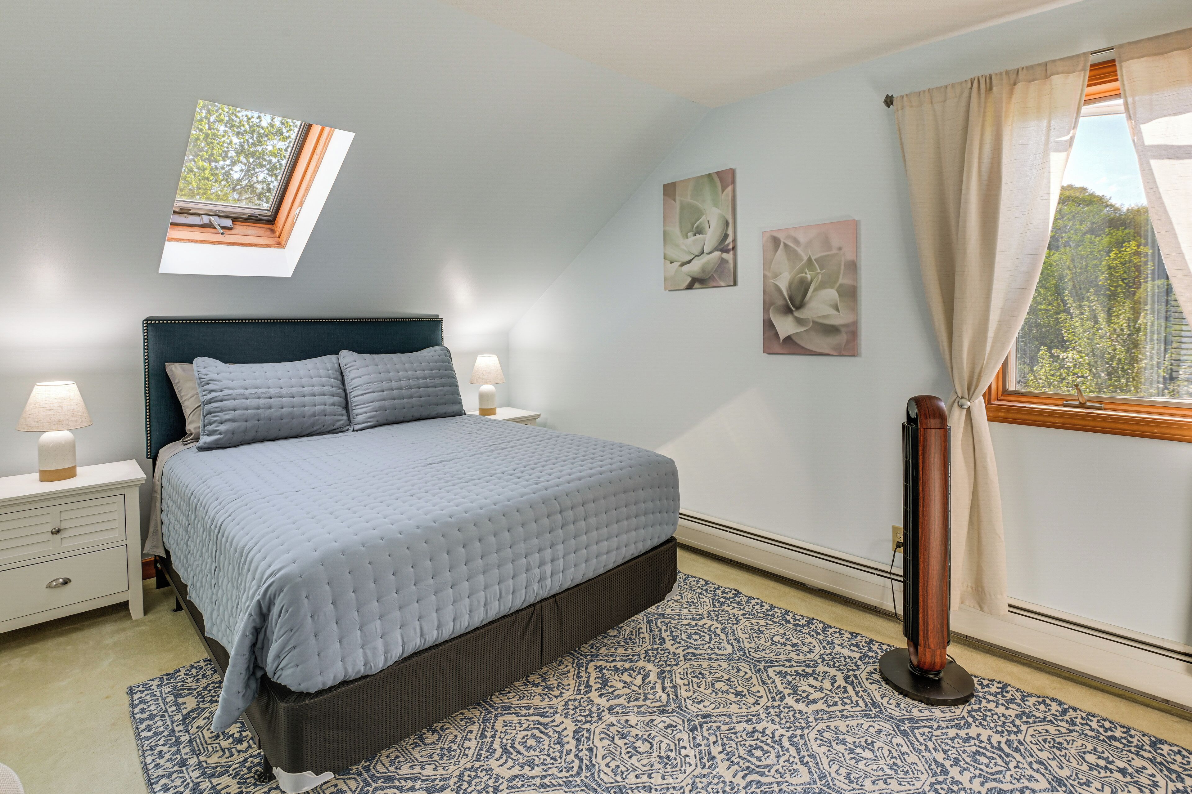 A bedroom with a bed, nightstands, a window with curtains, and wall art.