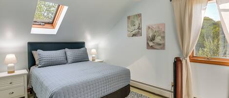 A bedroom with a bed, nightstands, a window with curtains, and wall art.