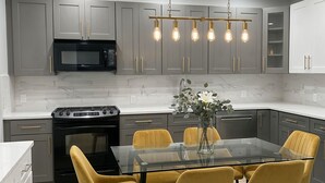 A modern kitchen with grey cabinets, a black microwave, a gas stove, and a glass dining table with yellow chairs.