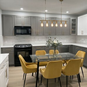 A modern kitchen with grey cabinets, a black microwave, a stove, and a glass dining table with yellow chairs. - Spacious 3BR Home • Free Parking • Convenient NYC Access • Perfect for Families (Yonkers)
