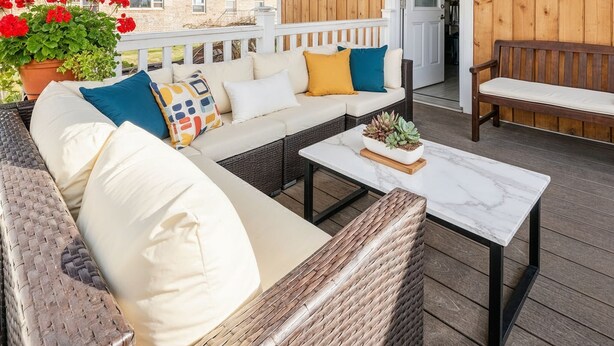 A covered outdoor seating area with a sofa, cushions, a coffee table, and string lights.