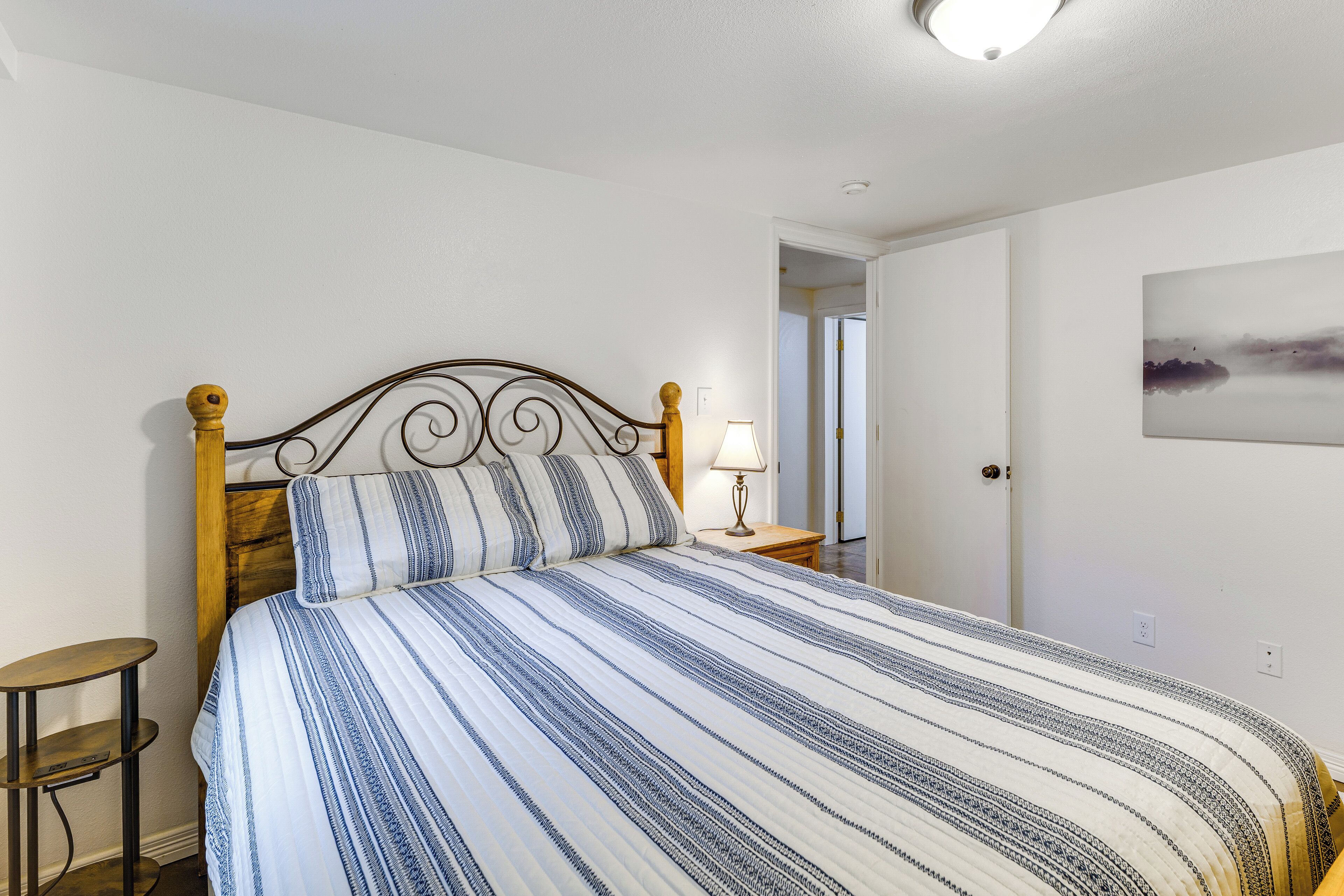 A bed with a striped bedspread, a wooden headboard, a bedside lamp, and a small table.