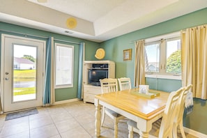 A dining area with a wooden table and chairs, a television, and a window with curtains.