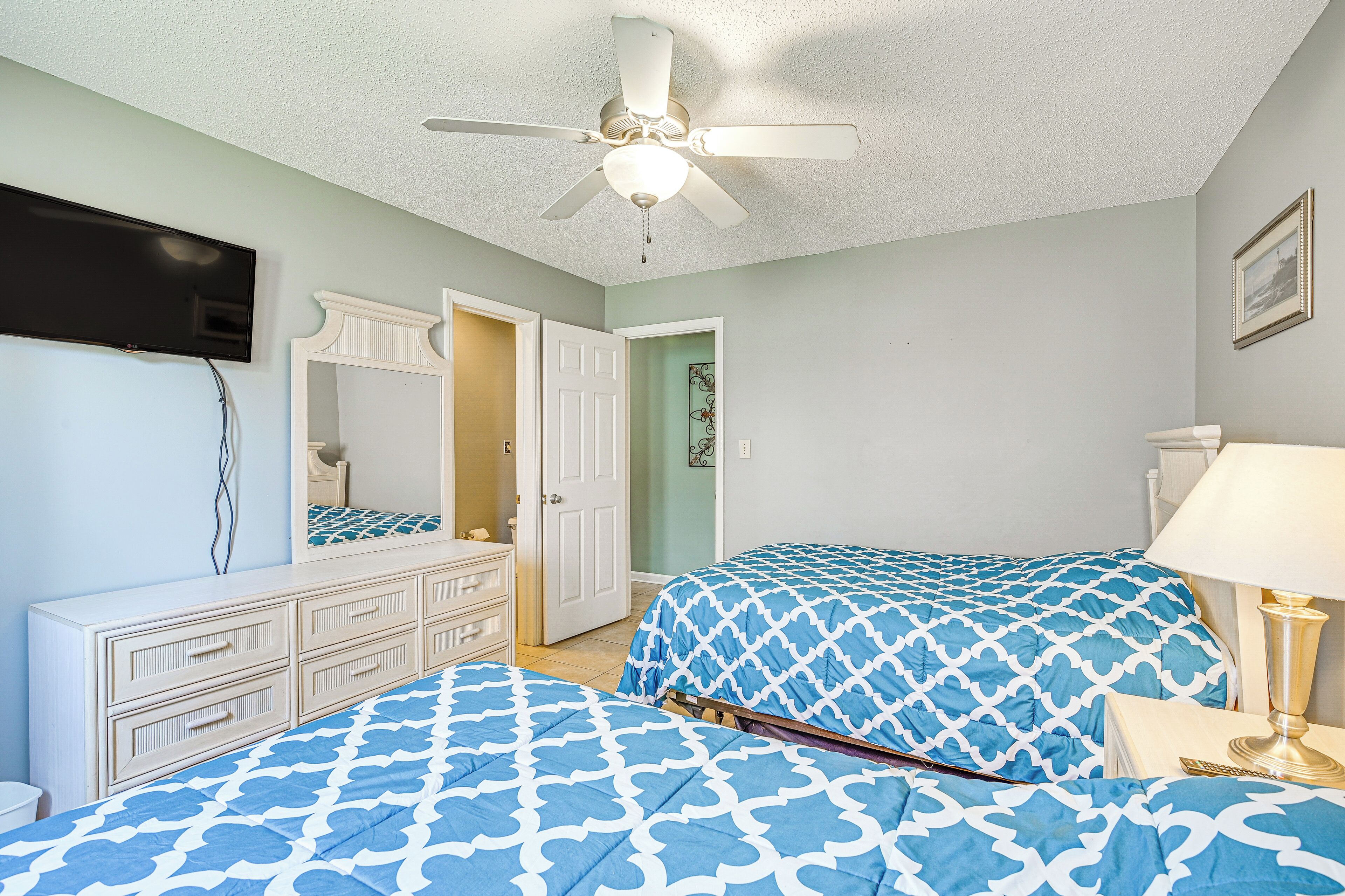 Une chambre à coucher comprenant un lit, une commode, un ventilateur de plafond et un téléviseur.