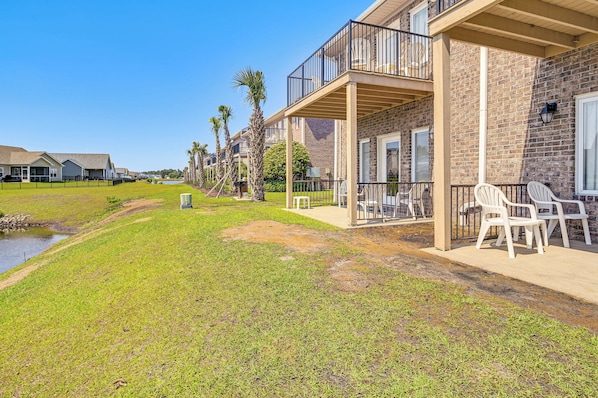 A residential building with a balcony, outdoor seating, and a grassy area with a small pond.