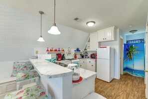 A compact kitchen with white cabinets, a central island, pendant lighting, and a tropical-themed wall mural. - Walk to Waves! Surfside Beach House w/ Ocean View (Freeport)