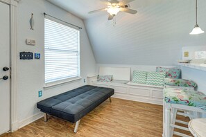 A room with a bed, a bench, a ceiling fan, a window with blinds, and a small table with a lamp. - Walk to Waves! Surfside Beach House w/ Ocean View (Freeport)