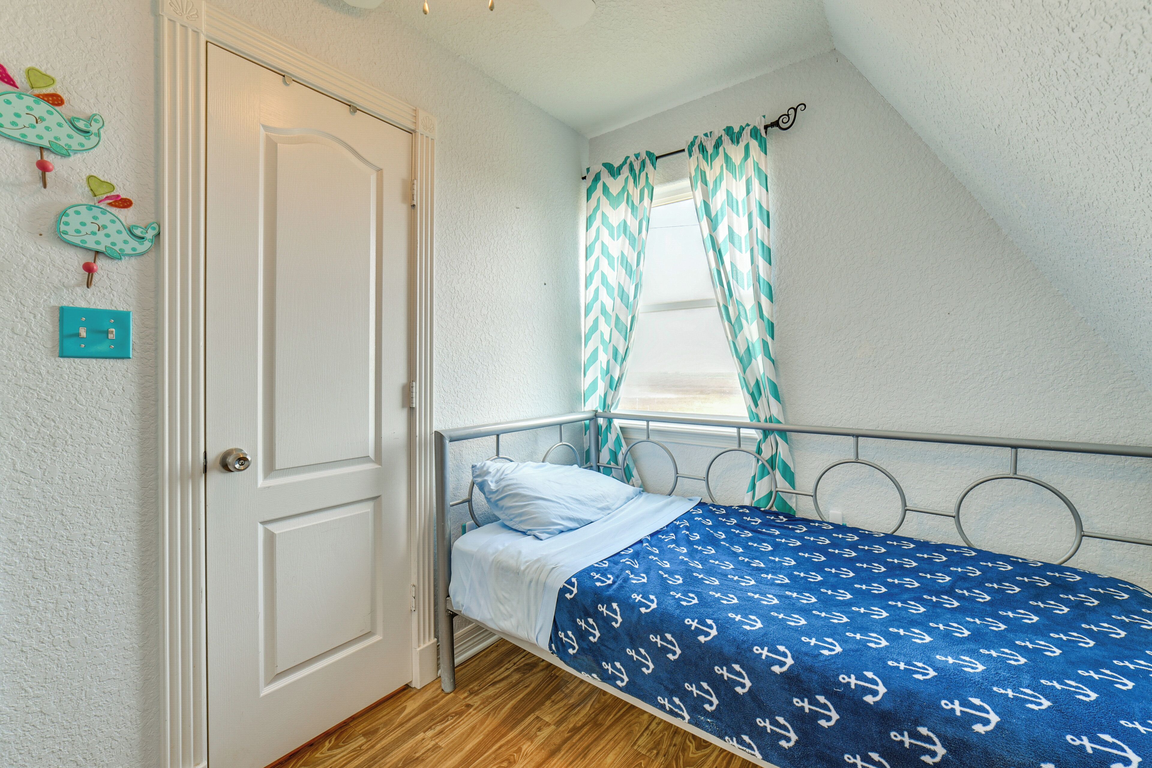 Een eenpersoonsbed met een bedsprei met een patroon, een witte deur en een raam met ruitvormige gordijnen.