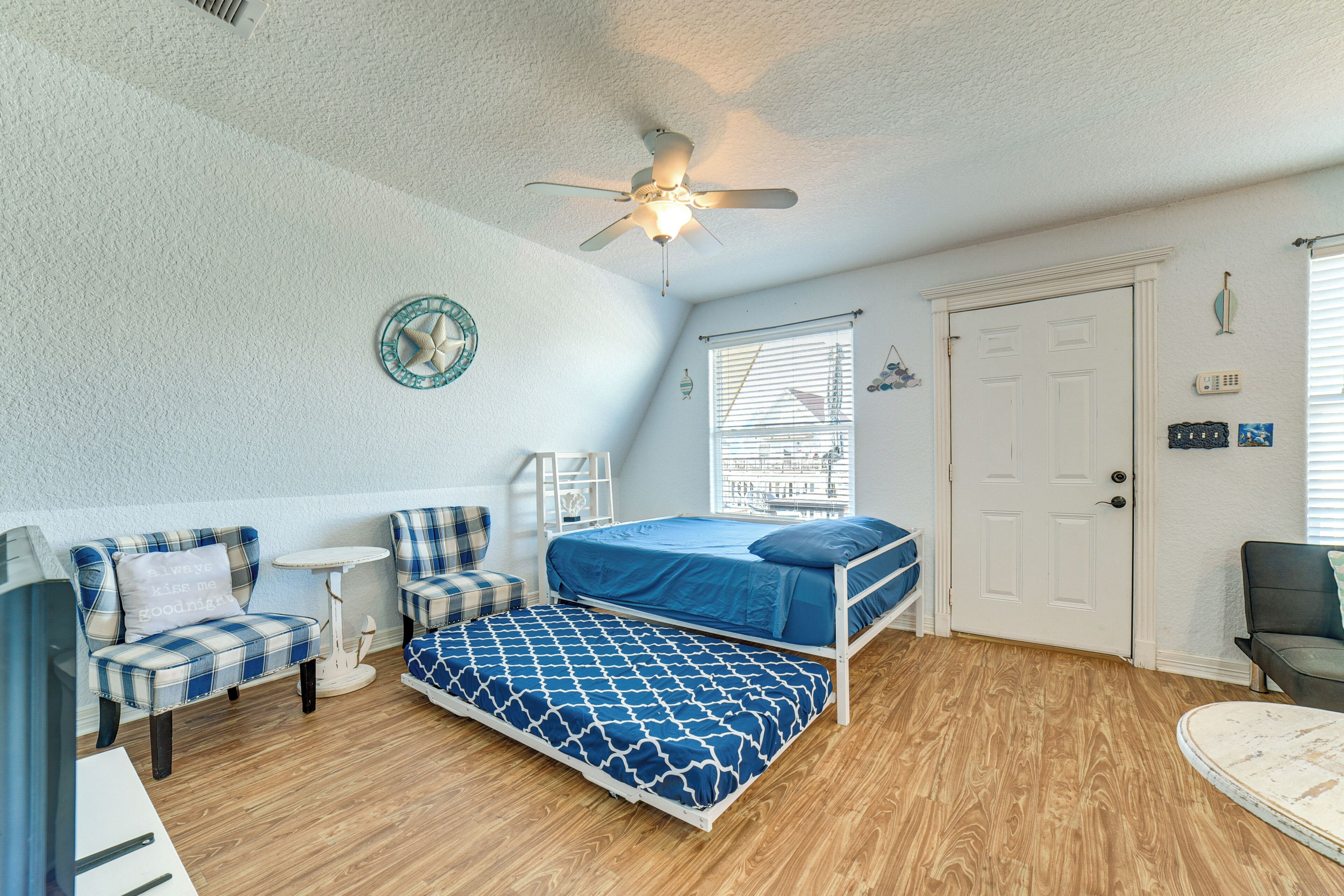 Une chambre à coucher avec un lit, une chaise, une petite table, un ventilateur de plafond et une porte.