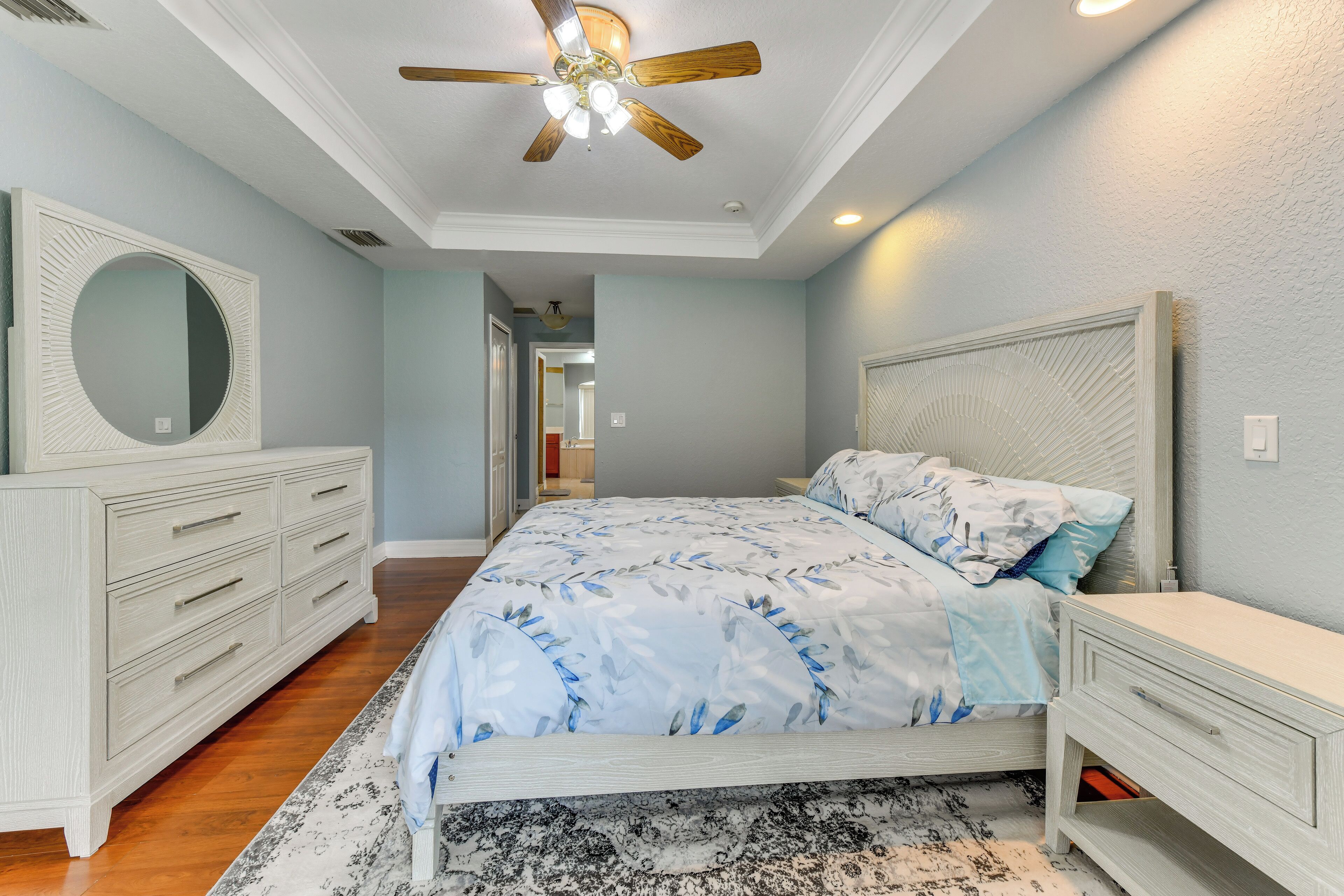 A bedroom with a bed, a dresser, a mirror, and a ceiling fan.