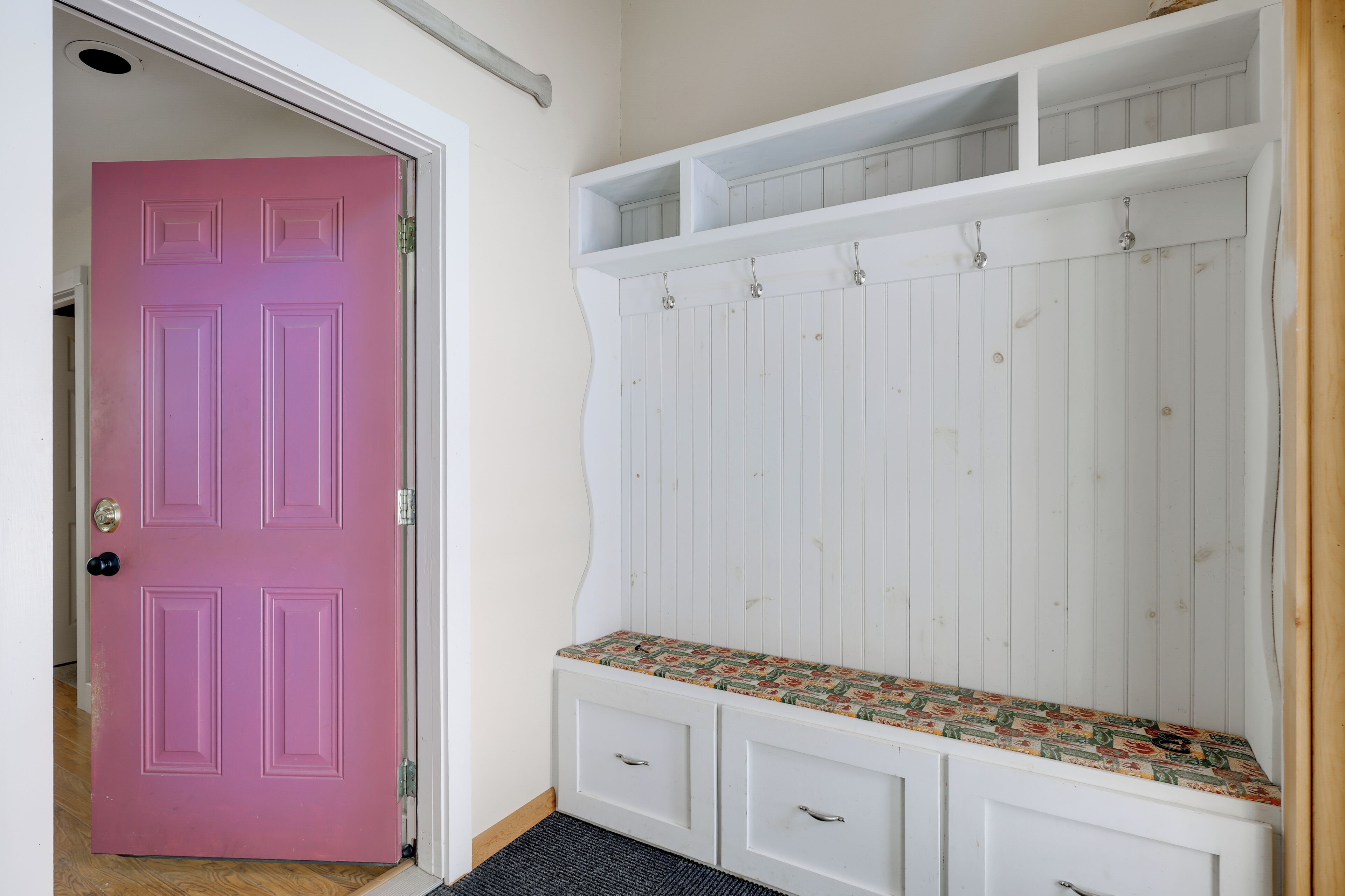 Een roze deur, een witte bank met een gestreept zitvlak en een witte muur met een plank.