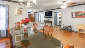 A dining area with a glass table, wooden chairs, a vase with flowers, a ceiling fan, and a TV in the background. - Pets Welcome! Comfortable and Spacious! Sleeps 6 (Frankston)