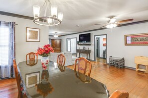 A dining area with a glass table, wooden chairs, a vase with flowers, a ceiling fan, and a TV in the background. - Pets Welcome! Comfortable and Spacious! Sleeps 6 (Frankston)