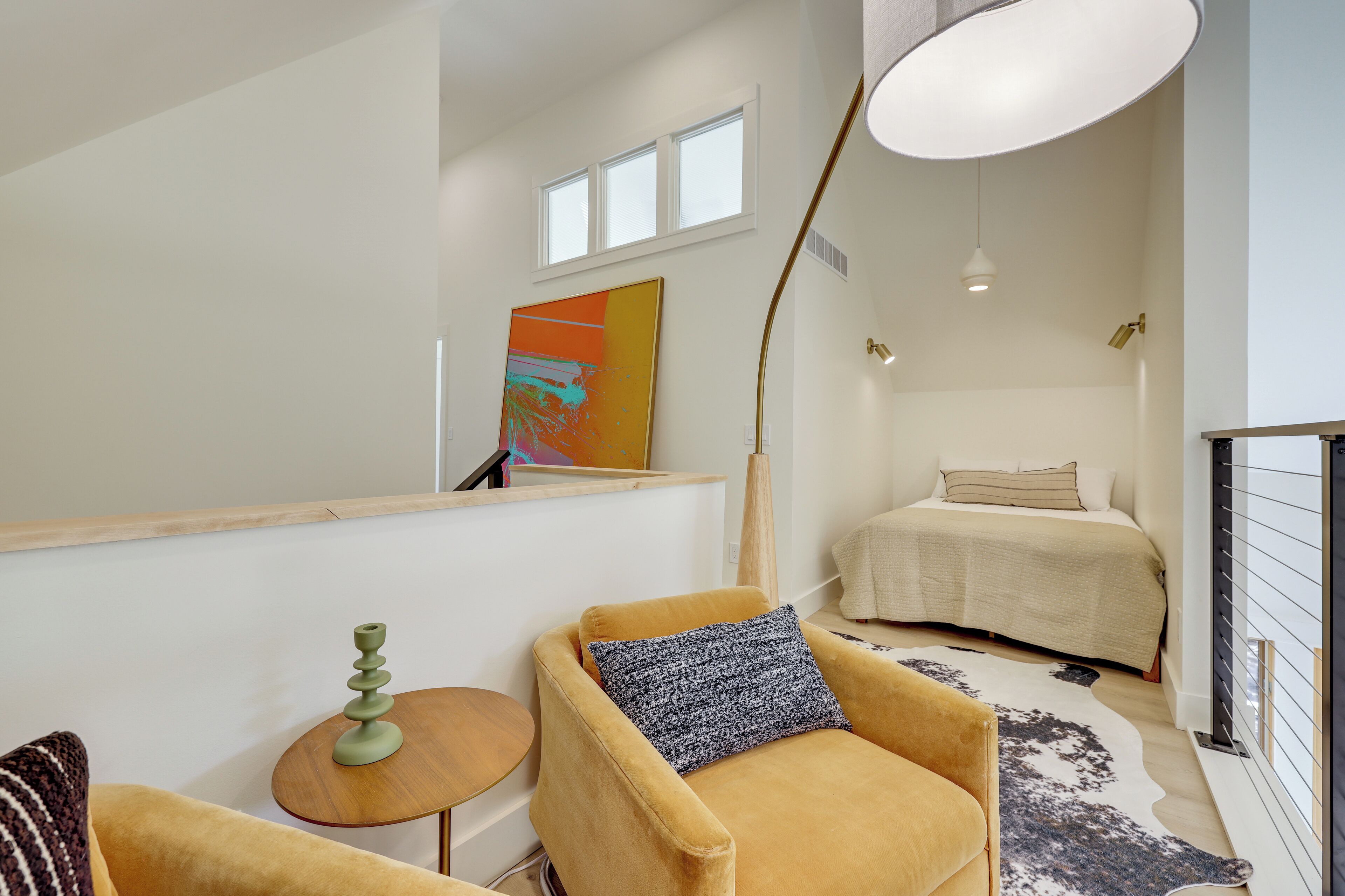 A modern bedroom with a bed, a chair, a small table, and a painting on the wall.
