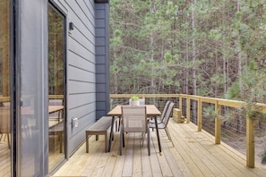 Terraza con mesa y sillas, con vista a un bosque.
