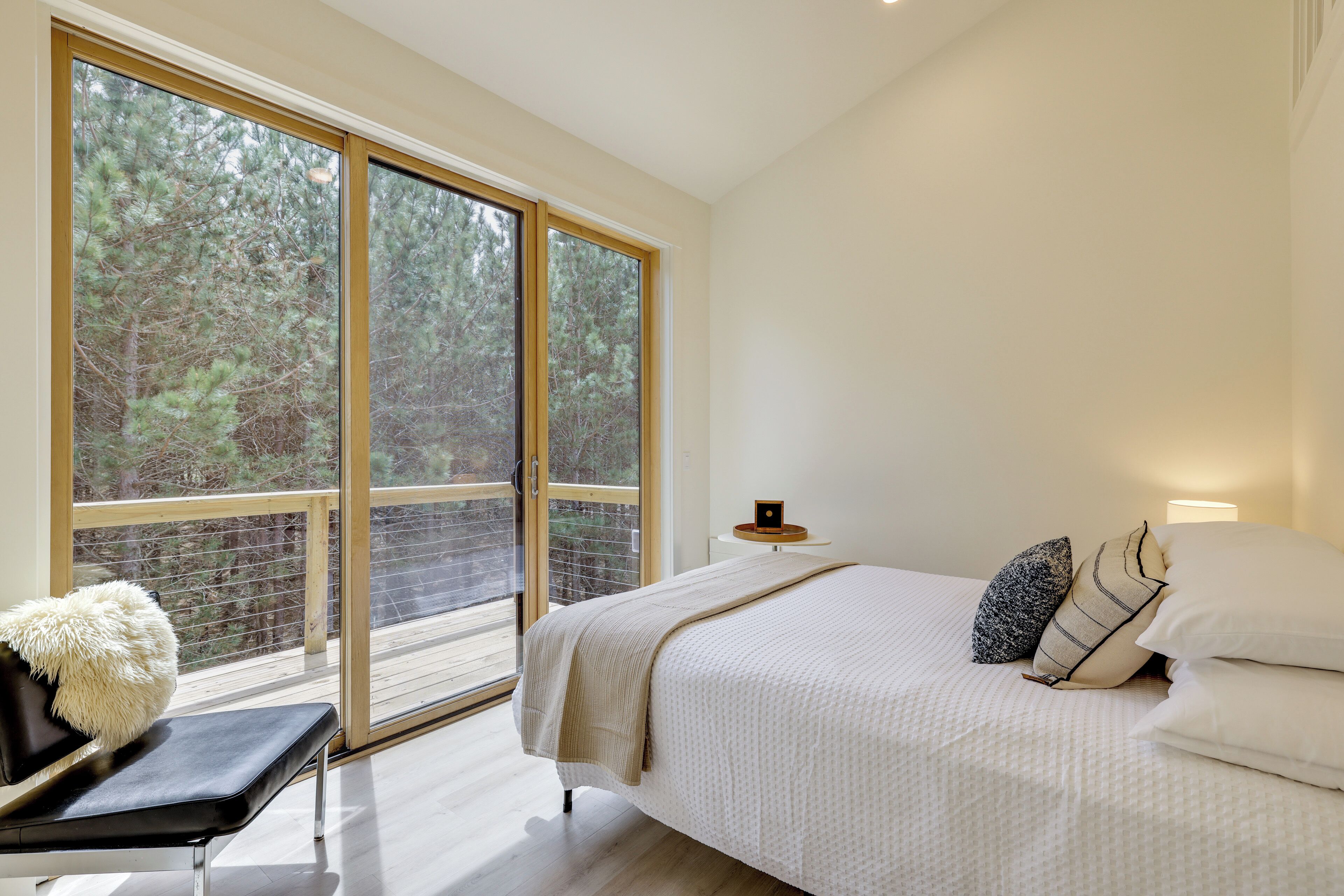 Ein Schlafzimmer mit großem Fenster, einem Bett mit Kissen, einer Bank und einem kleinen Tisch mit Lampe.