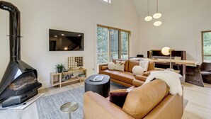 Una sala de estar moderna con chimenea, sofá de cuero, mesita de madera y ventanas amplias.