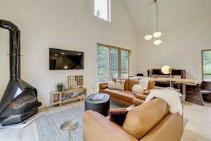 Una sala de estar moderna con chimenea, sofá de cuero, mesita de madera y ventanas amplias.