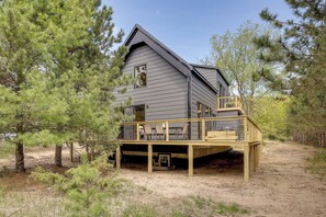 A two-story cabin with a deck, surrounded by trees.