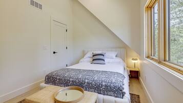A bedroom with a bed, bedside table, lamp, and a window with a view.