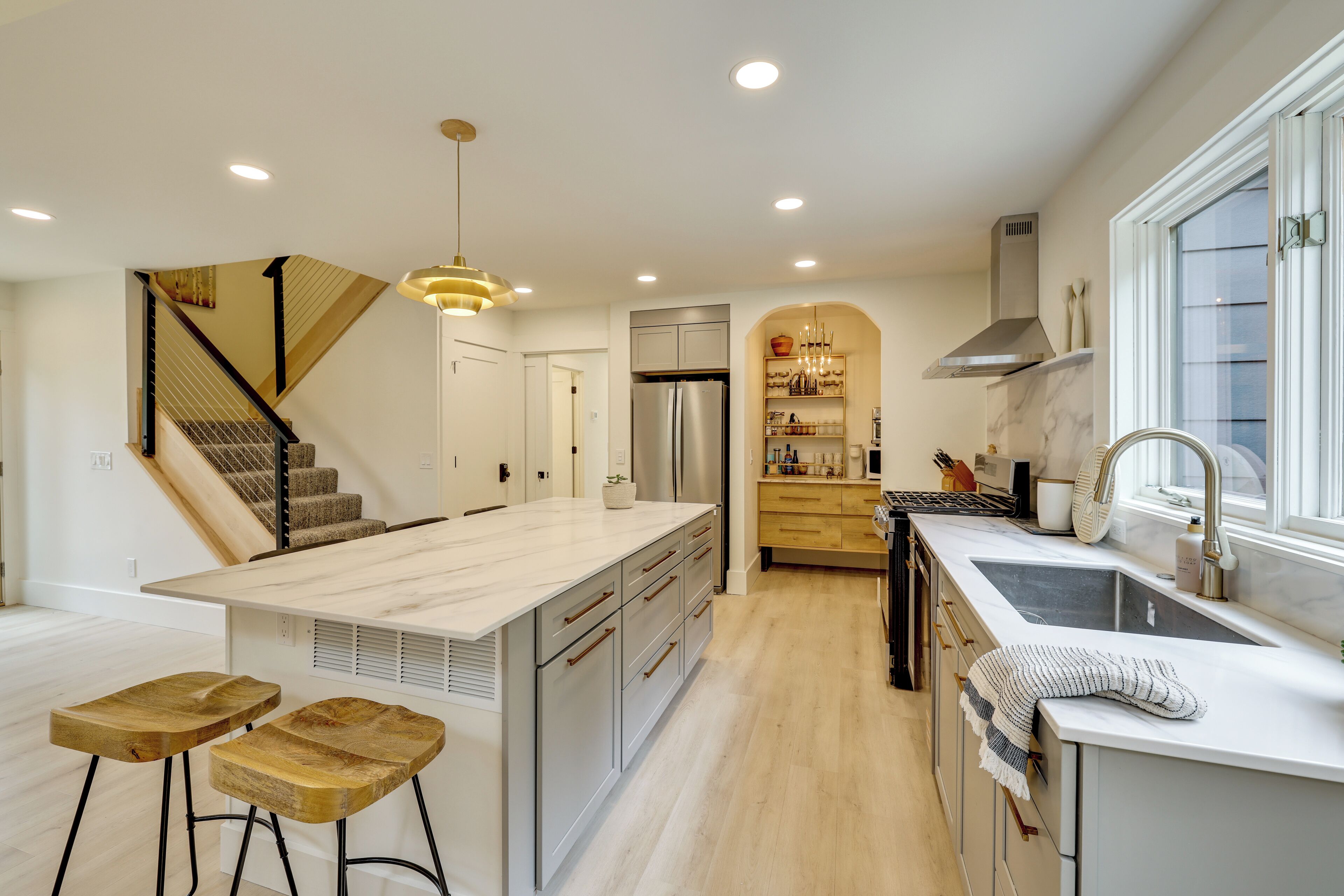 A modern kitchen with a central island, bar stools, a built-in stove, and a large window.