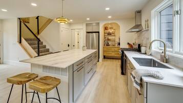 A modern kitchen with a central island, bar stools, a built-in stove, and a large window.