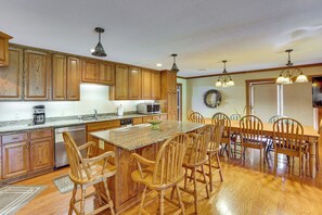 Una cocina con armarios de madera, encimera de granito, una mesa de comedor con sillas e iluminación colgante.