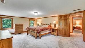 Un dormitorio con cama, cómoda, mesitas de noche y una puerta que da a otra habitación.