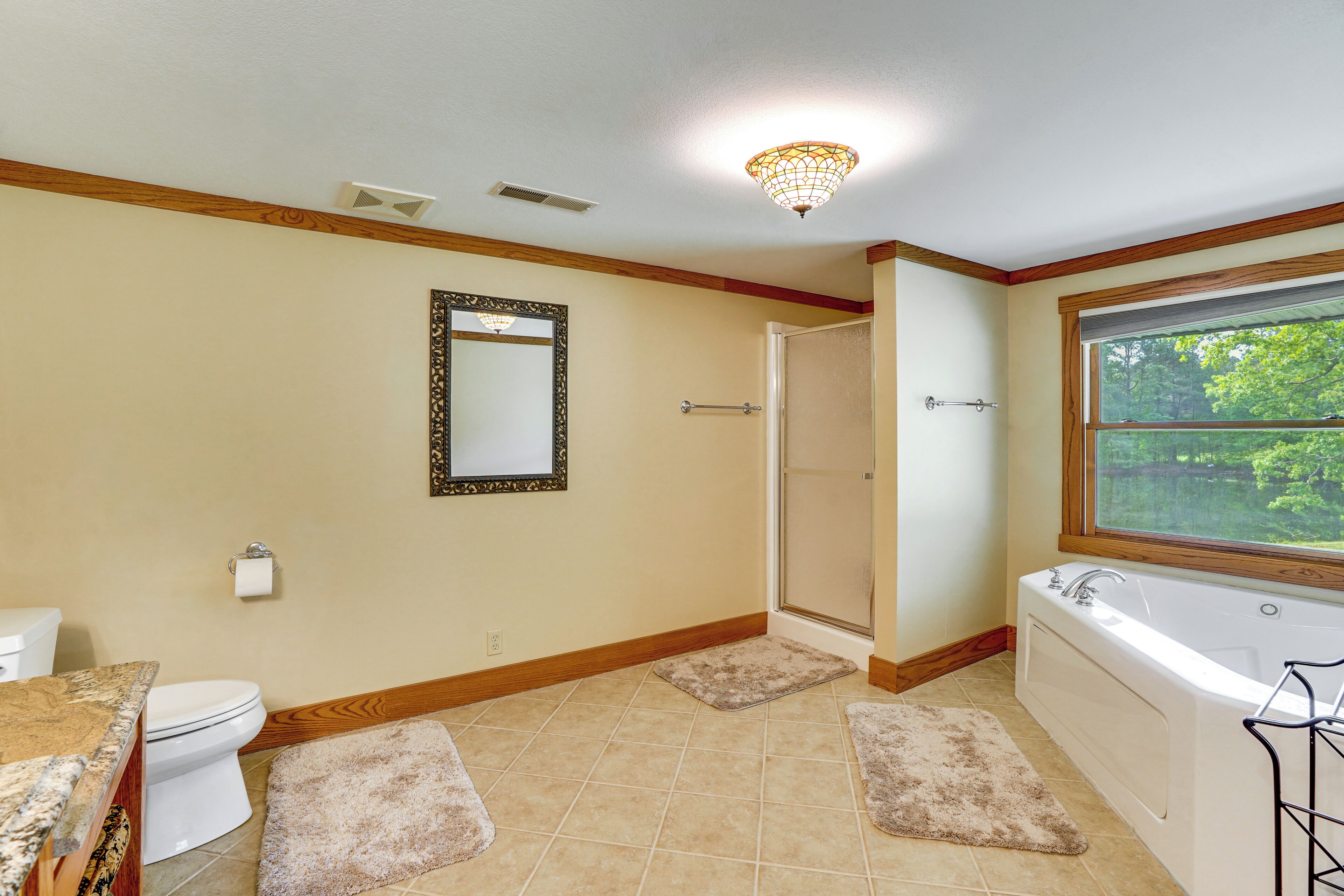 A bathroom with a toilet, sink, bathtub, shower, and a large window.