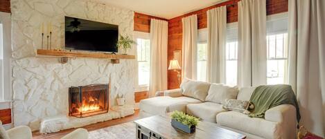 A living room with a stone fireplace, a sofa, a coffee table, and a television mounted on the wall.