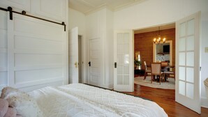 A bedroom with a large bed, a wooden floor, and a dining area with a chandelier. - Pet-friendly Historic Home: Downtown Breaux Bridge (Breaux Bridge)
