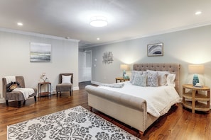 A bedroom with a large bed, two chairs, a rug, and a nightstand with a lamp.