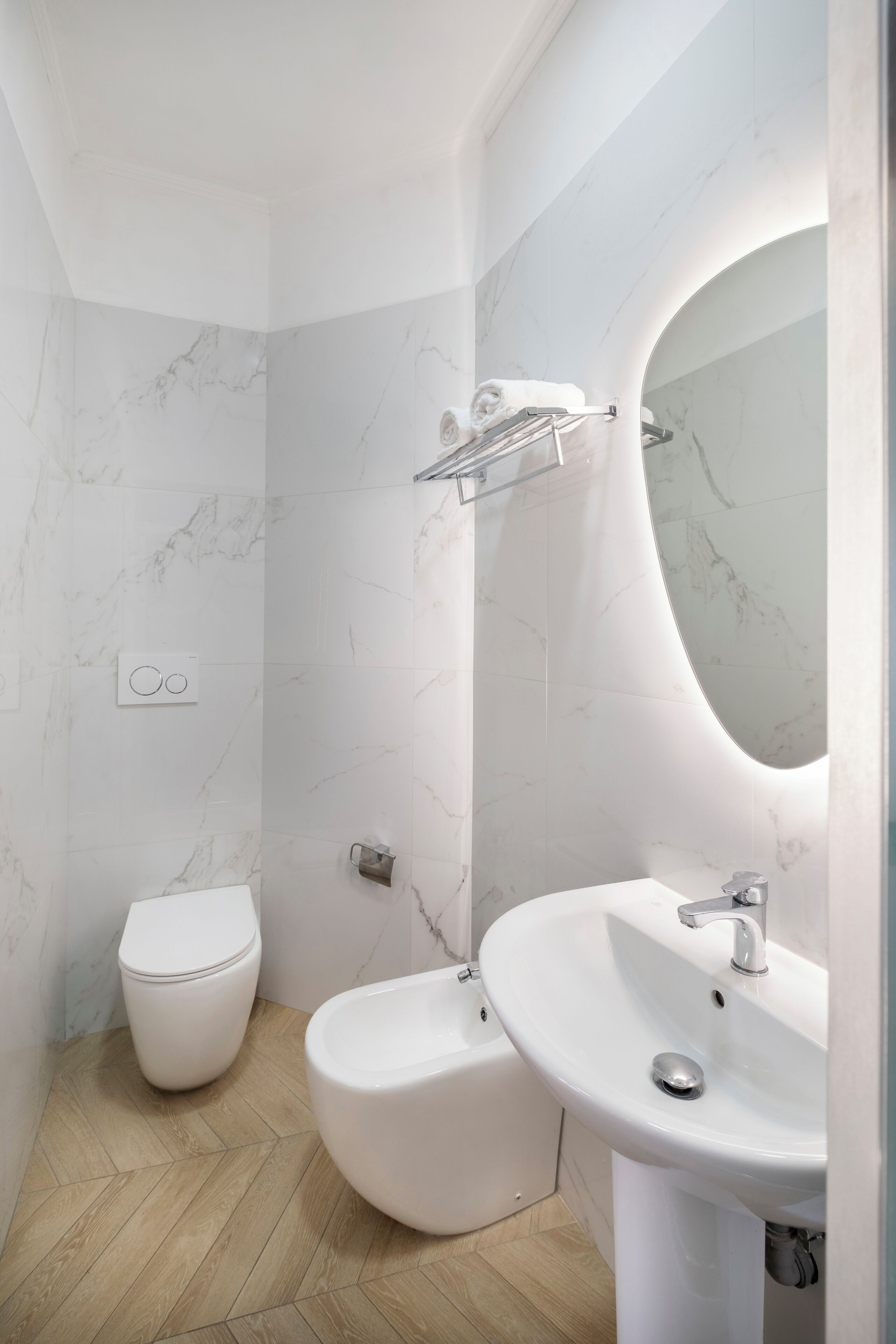 A bathroom with a toilet, bidet, and sink, marble walls, and a herringbone floor pattern.