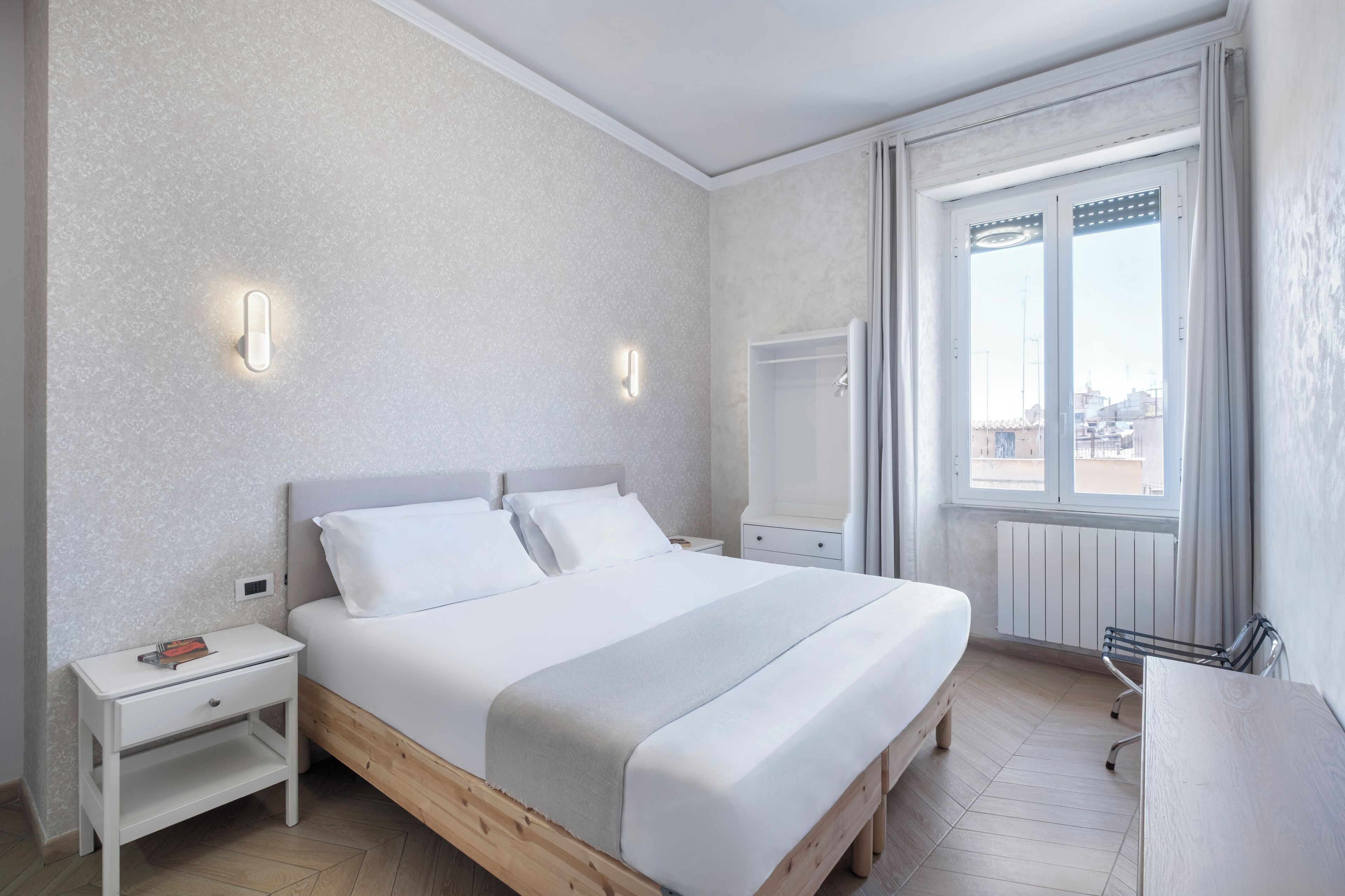 A modern bedroom with a wooden bed, white bedding, a nightstand, a desk, and a window with a view.