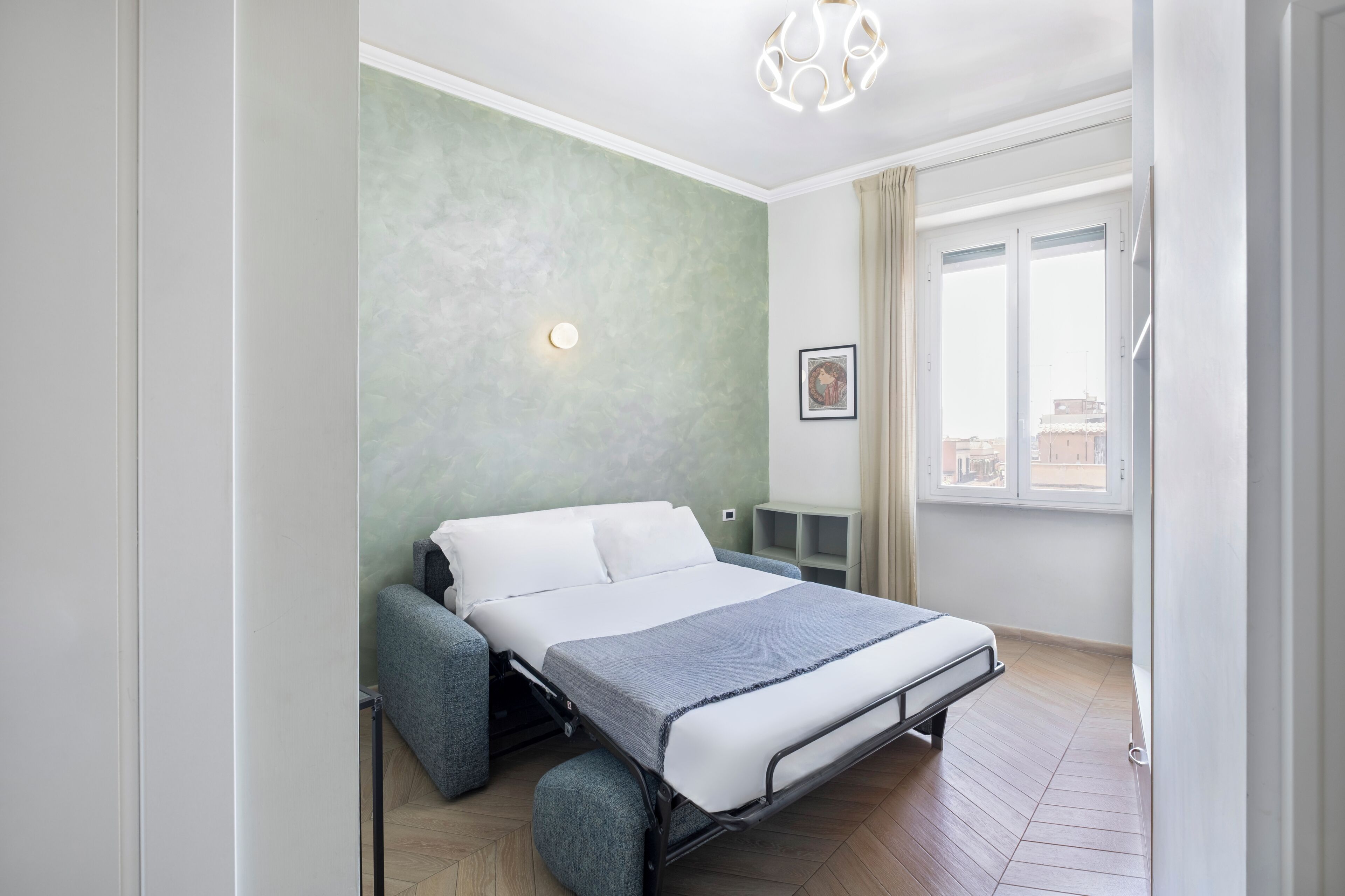 Un dormitorio pequeño con cama, una pared de acento verde, una ventana con cortinas y una lámpara en el techo.