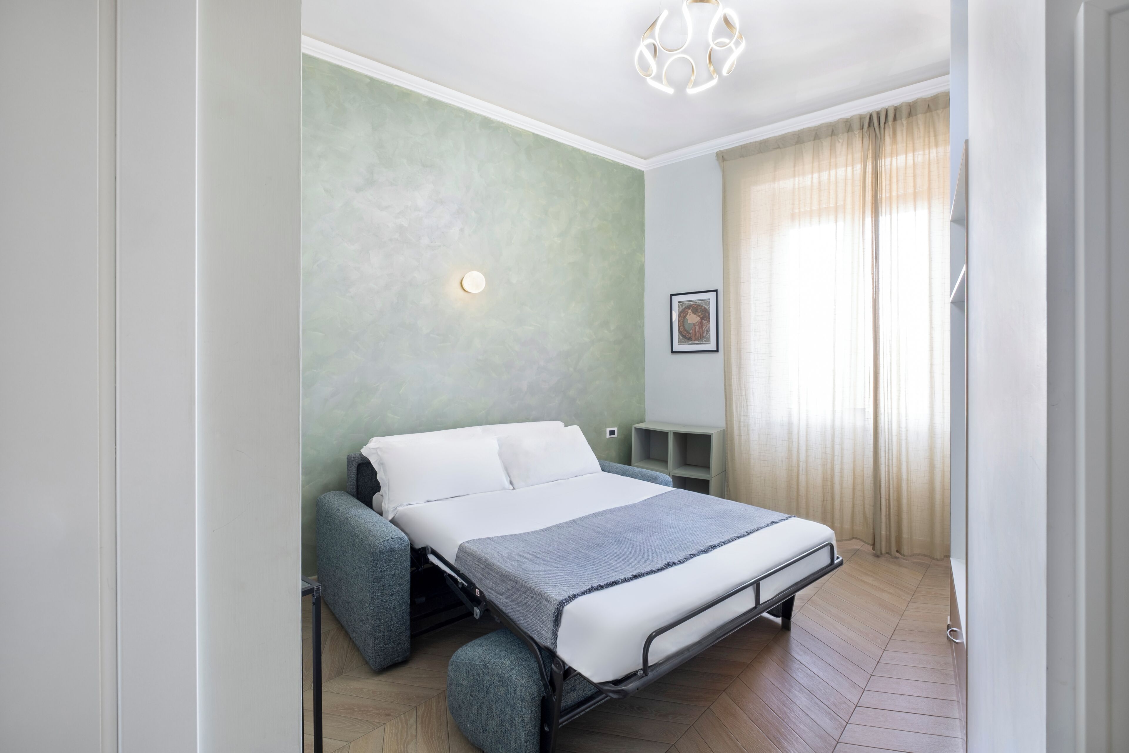 A modern bedroom with a bed, a nightstand, a wall-mounted light, and a window with curtains.