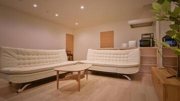 A modern living room with two sofas, a small table, and a kitchenette area with appliances.