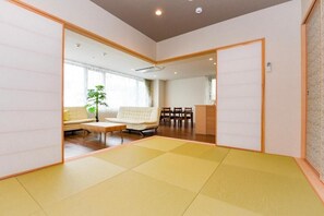 Una habitación tradicional japonesa con suelo de tatami, un sofá, una mesa de centro y un comedor con sillas.