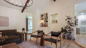 Ett vardagsrum med en brun soffa, två fåtöljer, ett soffbord, en kristallkrona och en stor växt.