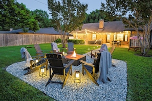 A backyard with a fire pit, seating, and string lights. - Luxury 4 Bedroom, 2.5 Bath retreat ideal location, just 9 minutes from AT&T Stadium! Movie Room, Hot Tub, Fire Pit, Coffee Bar, Outdoor Dining and seating, Ping Pong, Games, Bunk Room and Fireplace. (Grand Prairie)