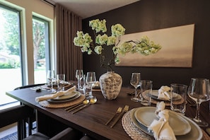 A dining table set with plates, cutlery, and glasses, a vase with flowers, and a painting on the wall. - Luxury 4 Bedroom, 2.5 Bath retreat ideal location, just 9 minutes from AT&T Stadium! Movie Room, Hot Tub, Fire Pit, Coffee Bar, Outdoor Dining and seating, Ping Pong, Games, Bunk Room and Fireplace. (Grand Prairie)