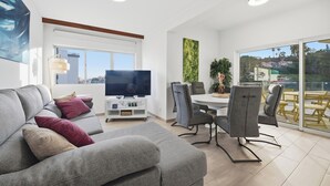 A modern living room with a grey sofa, a flat-screen TV, and a dining area with chairs and a table. - Little Paradise - Funchal (Funchal)
